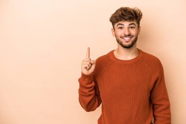 Young arab man isolated on beige background showing number one with finger.