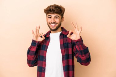 Young arab man isolated on beige background cheerful and confident showing ok gesture.