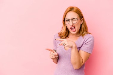 Pembe arka planda izole edilmiş genç beyaz kadın işaret parmaklarıyla fotokopi alanını işaret ederek heyecan ve arzusunu ifade ediyor..