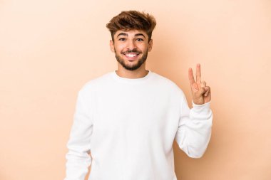 Young arab man isolated on beige background joyful and carefree showing a peace symbol with fingers.