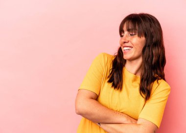 Pembe arka planda izole edilmiş genç Arjantinli kadın kollarını kavuşturarak gülümsüyor..