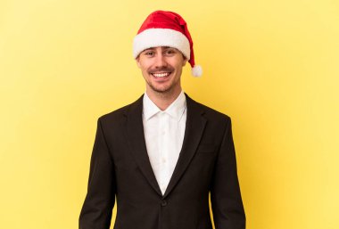 Yeni yılı kutlayan beyaz bir genç adam sarı arka planda izole edilmiş bir Noel şapkası takıyor.