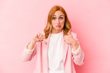 Pembe arka planda izole edilmiş genç beyaz kadın baş parmağını kaldırıyor ve baş parmağını aşağı gösteriyor, zor seçim kavramı.