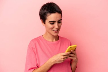 Pembe arka planda cep telefonu tutan beyaz bir kadın.