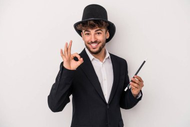 Young arab wizard man holding a wand isolated on white background cheerful and confident showing ok gesture.