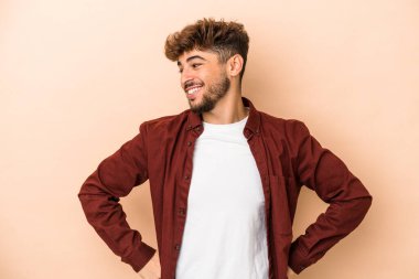 Young arab man isolated on beige background laughs happily and has fun keeping hands on stomach.