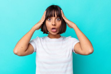 Mavi arka planda izole edilmiş genç melez kadın zaferi ya da başarıyı kutluyor, şaşırıyor ve şok oluyor..