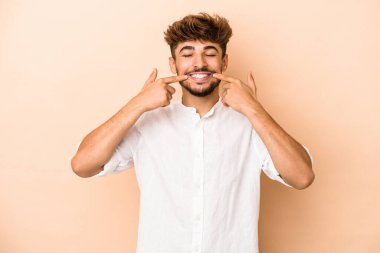 Young arab man isolated on beige background smiles, pointing fingers at mouth.