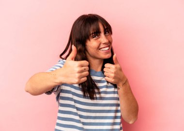 Arjantinli genç bir kadın pembe arka planda izole edilmiş. Baş parmağını kaldırıyor, gülümsüyor ve kendinden emin..