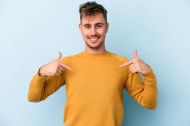 Kafkasyalı genç adam mavi arka planda izole edildi. Parmakları aşağıda, olumlu bir his var..