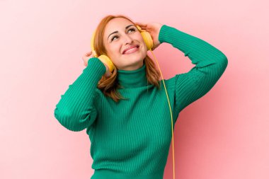 Pembe arka planda izole edilmiş müzik dinleyen beyaz bir kadın.