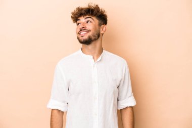 Genç Arap adam bej arka planda izole edilmiş gevşemiş ve mutlu bir şekilde gülüyor, boynunu uzatmış dişlerini gösteriyor..