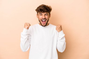 Genç Arap adam bej arka planda izole edilmiş tasasız ve heyecanlı tezahüratlar yapıyor. Zafer konsepti.