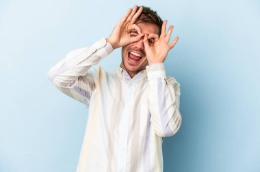 Mavi arka planda izole edilmiş genç beyaz adam gözlerinde sorun olmadığını gösteriyor.