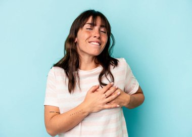 Mavi arka planda izole edilmiş genç Arjantinli kadın avuçlarını göğsüne bastıran dostça bir ifadeye sahip. Aşk konsepti.