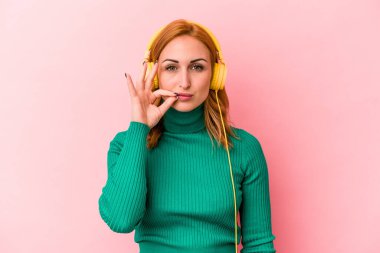 Pembe arka planda izole edilmiş müzik dinleyen beyaz bir kadın. Parmakları dudaklarında bir sır saklıyor..