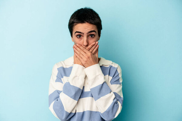 Young caucasian woman isolated on blue background shocked covering mouth with hands.