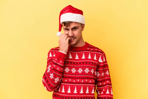 若いです白人男性祝うクリスマスは黄色の背景に隔離された爪をかむ 神経と非常に不安 — ストック写真