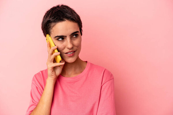 Молодая белая женщина держит мобильный телефон изолирован на розовом фоне