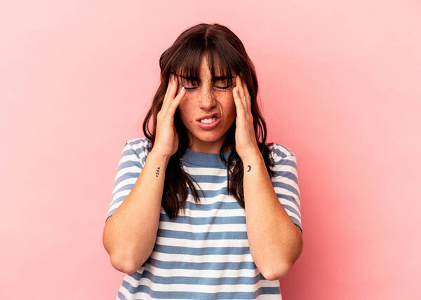 Young Argentinian woman isolated on pink background having a head ache, touching front of the face.