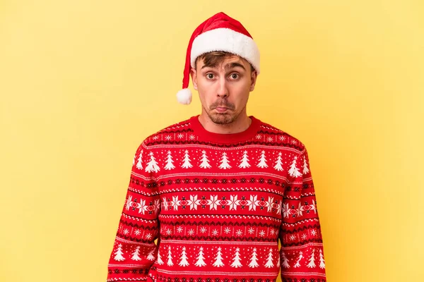 若いですCaucasian男祝いますクリスマス絶縁上の黄色の背景Shrugs肩とオープン目混乱 — ストック写真
