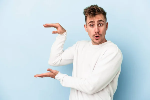 Joven Hombre Caucásico Aislado Sobre Fondo Azul Sorprendido Sorprendido Sosteniendo — Foto de Stock