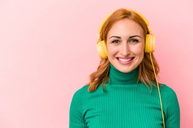 Pembe arka planda izole edilmiş müzik dinleyen beyaz bir kadın.