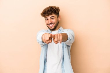 Young arab man isolated on beige background pointing to front with fingers.