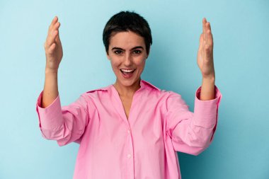 Mavi arka planda izole genç beyaz kadın zaferi ya da başarıyı kutluyor, şaşırıyor ve şok oluyor..