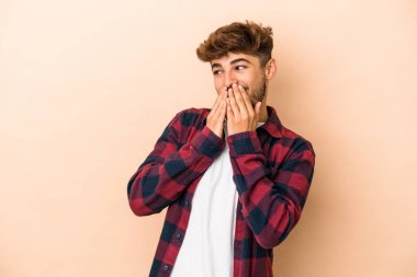 Young arab man isolated on beige background laughing about something, covering mouth with hands.