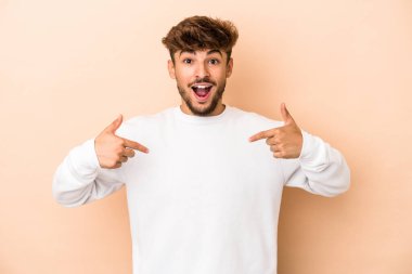 Young arab man isolated on beige background surprised pointing with finger, smiling broadly.