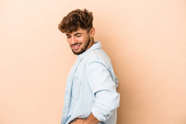 Genç Arap adam bej arka planda izole edilmiş, sırt ağrısı çekiyor..