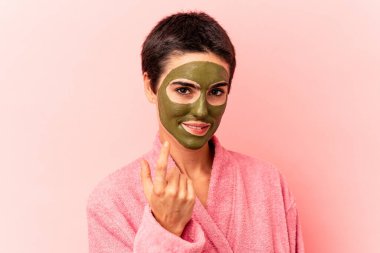 Pembe arka planda soyutlanmış yüz maskesi takan genç beyaz kadın sanki seni davet ediyormuş gibi seni işaret ediyor..