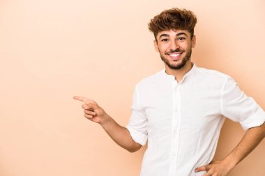Young arab man isolated on beige background smiling cheerfully pointing with forefinger away.
