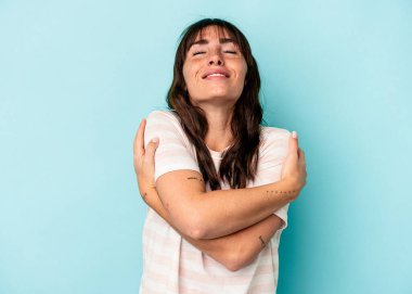 Arjantinli genç bir kadın mavi arka planda izole edilmiş, güler yüzlü ve mutlu..