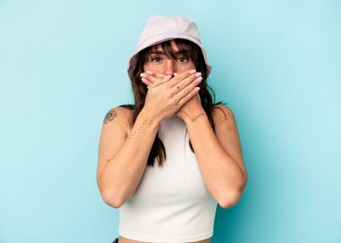 Arjantinli genç bir kadın mavi arka planda izole edilmiş, ağzı kapalı ve elleri endişeli görünüyor..