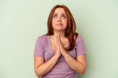 Yeşil arka planda izole edilmiş genç beyaz kadın el ele tutuşup dua ediyor, kendine güveniyor..