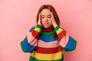 Genç beyaz kadın pembe arka planda izole edilmiş tapınaklara dokunuyor ve baş ağrısı çekiyor..