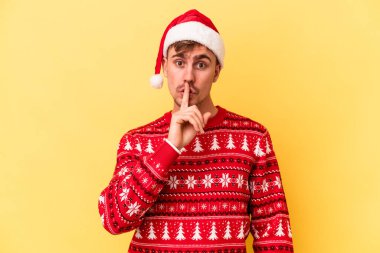 Sarı arka planda izole edilmiş bir şekilde Noel 'i kutlayan genç beyaz adam ya sır saklıyor ya da sessizlik istiyor..