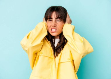 Arjantinli genç bir kadın mavi arka planda tek başına kulaklarını elleriyle kapatıyor..