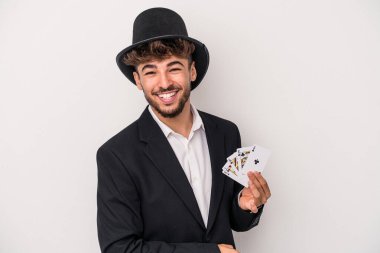 Young arab wizard man holding a magic cards isolated on white background laughing and having fun.