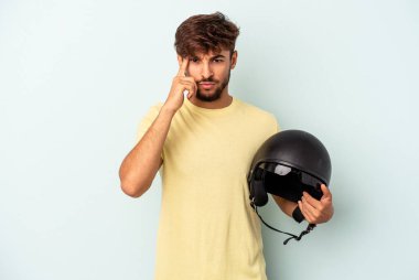 Young mixed race man holding motorcycle helmet isolated on blue background pointing temple with finger, thinking, focused on a task.