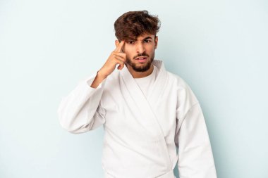 Young mixed race man doing karate isolated on blue background showing a disappointment gesture with forefinger.