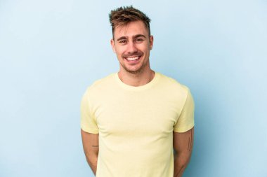 Mavi arka planda izole edilmiş genç beyaz adam mutlu, güler yüzlü ve neşeli.