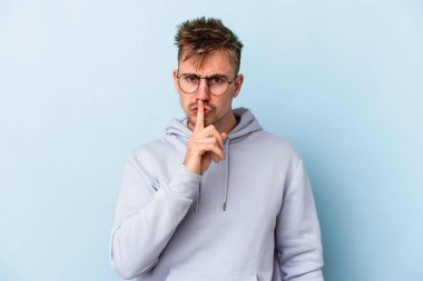 Mavi arka planda izole edilmiş genç beyaz bir adam ya sır saklıyor ya da sessizlik istiyor..