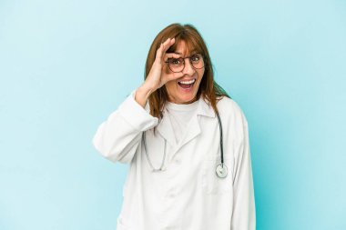 Middle age doctor woman isolated on pink background excited keeping ok gesture on eye.