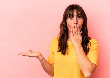 Pembe arka planda izole edilmiş genç Arjantinli kadın, avuç içinde fotokopi alanı bulundurmaktan etkilenmiş..