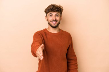 Young arab man isolated on beige background stretching hand at camera in greeting gesture.