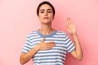 Beyaz bir kadın mavi arka planda izole edilmiş yemin ediyor, elini göğsüne koyuyor..