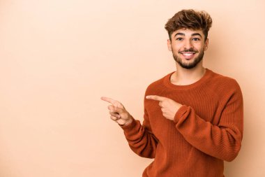 Young arab man isolated on beige background excited pointing with forefingers away.